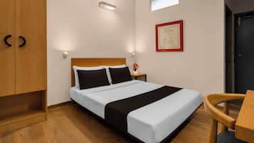 A hotel room with a bed, wooden wardrobe, bedside table, and a small window.