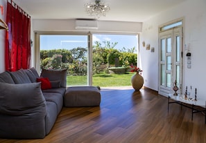 Ein modernes Wohnzimmer mit einem grauen Sofa, einem großen Fenster und Blick auf einen Garten.