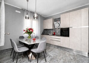 Une cuisine moderne avec des meubles gris, un plan de travail en marbre et un coin repas comprenant une table et des chaises.