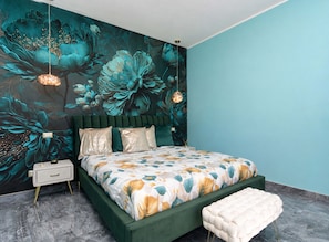 Ein Schlafzimmer mit einer großen Blumenwand, einem mit grünem Stoff bezogenen Bett, einem Nachttisch mit Lampe und einer Bank.