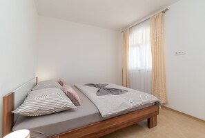 Een eenpersoonsbed met beddengoed met een patroon en een houten hoofdbord in een kamer met witte muren en een raam met dunne gordijnen.