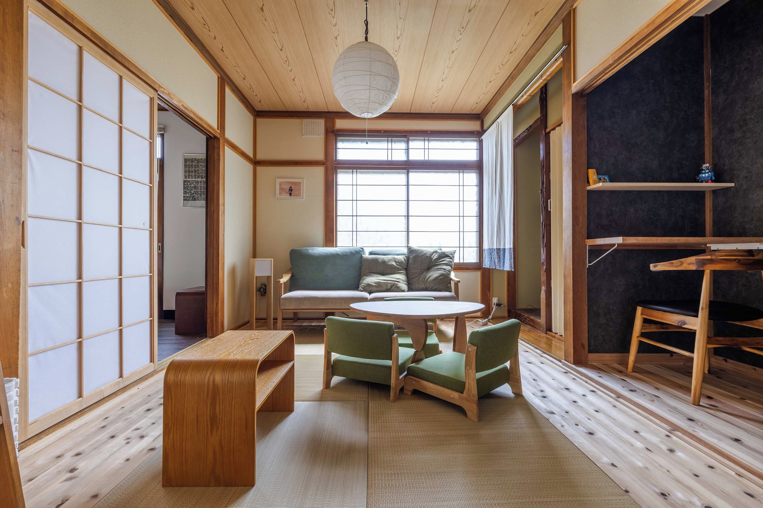 A traditional Japanese room with tatami flooring, a low table with chairs, a sofa, and a large window.