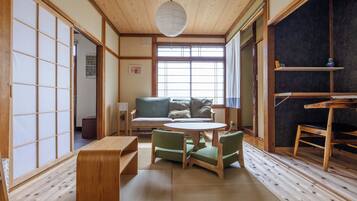 A traditional Japanese room with tatami flooring, a low table with chairs, a sofa, and a large window.