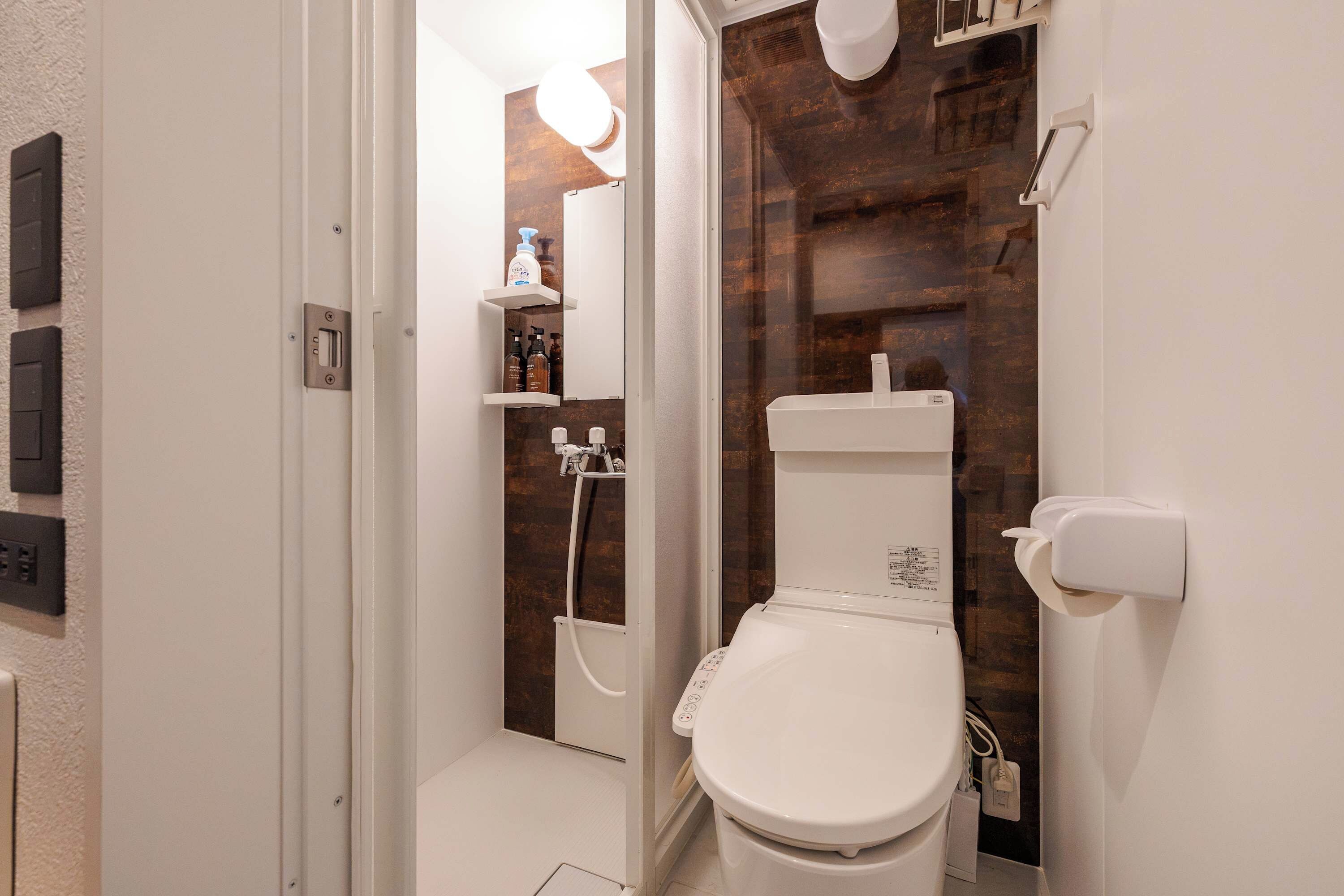 A modern bathroom with a toilet, a shower, and a sink. There are toiletries on the wall and a towel rack.