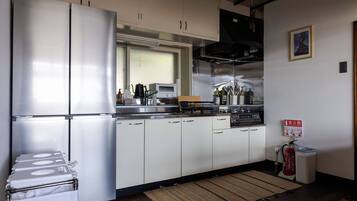 A compact kitchen with a stainless steel refrigerator, a microwave, and a stove. There is a fire extinguisher mounted on the wall and a small rug on the floor.
