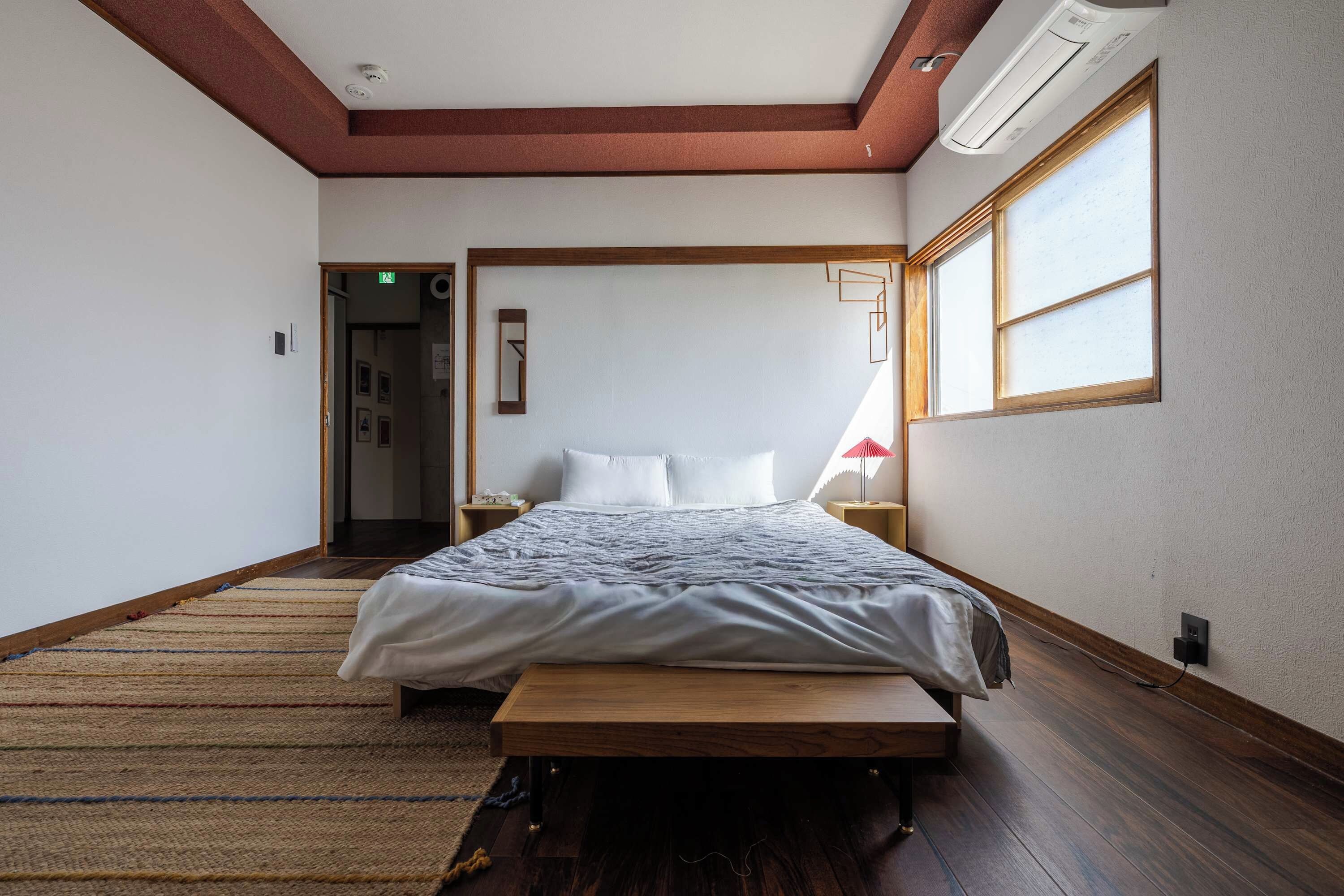 A bedroom with a bed, a bedside table, a nightstand, a window, and a door.