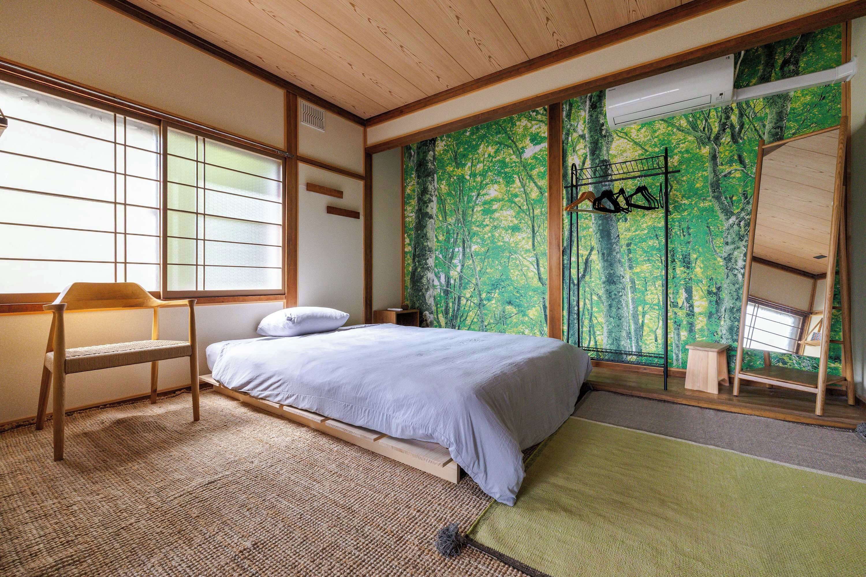 A bedroom with a bed, a chair, a desk, and a large window.