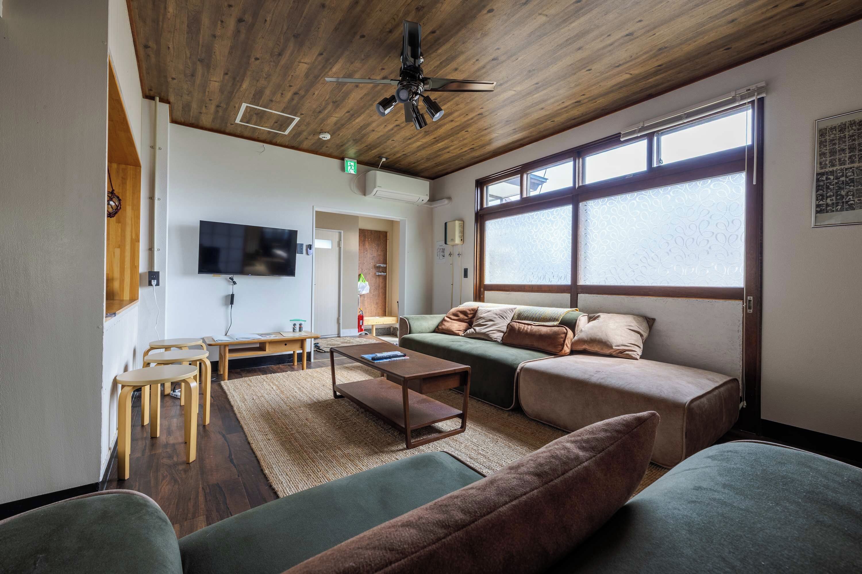 A modern living room with a wooden ceiling, a flat-screen TV, a sofa, a coffee table, and a large window.