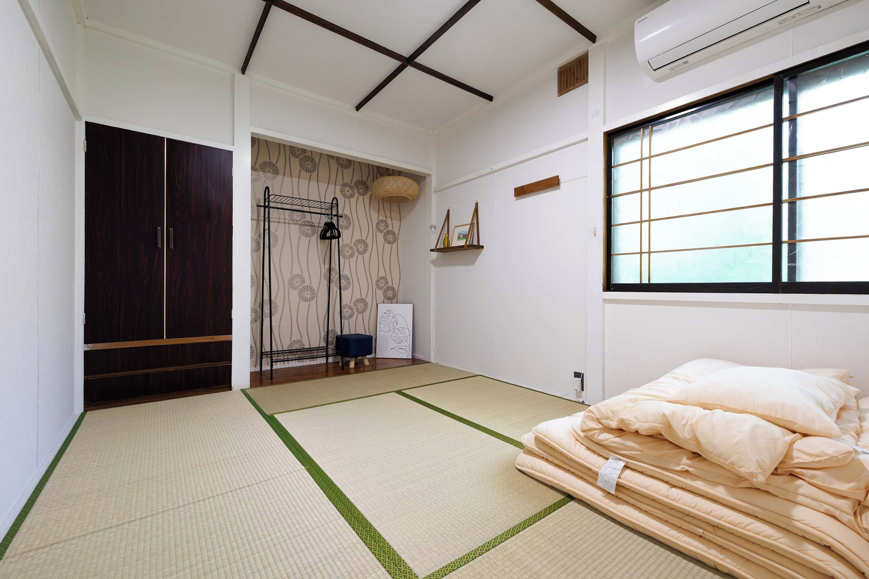 A room with tatami flooring, a bed with pillows, a wardrobe, a shelf with decorative items, and a window with a grid pattern.