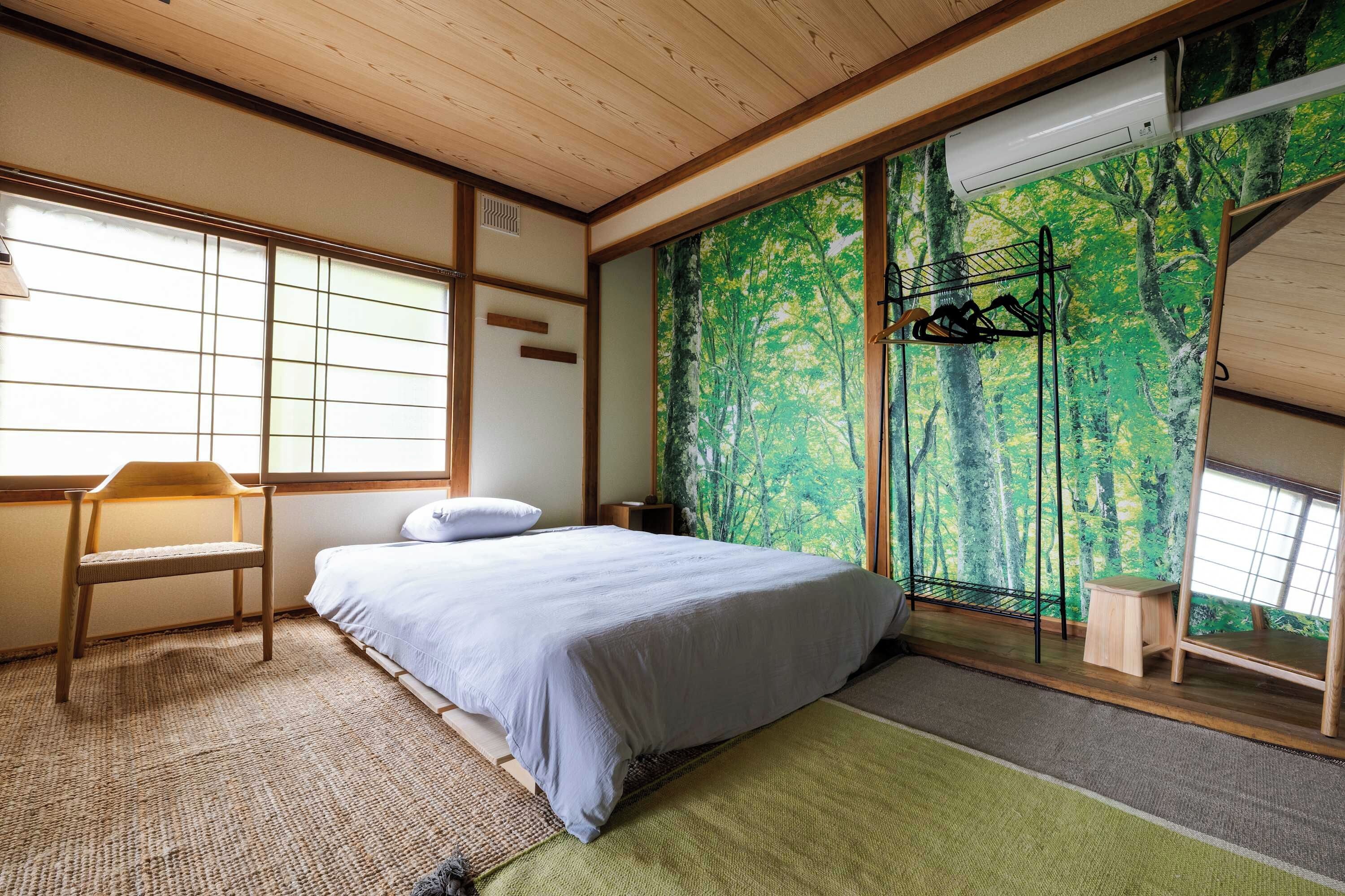 A room with a bed, a chair, a window, and a wall with a forest mural.