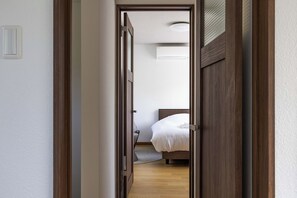 Un couloir étroit mène à une chambre à coucher équipée d’un lit et d’un ventilateur de plafond.