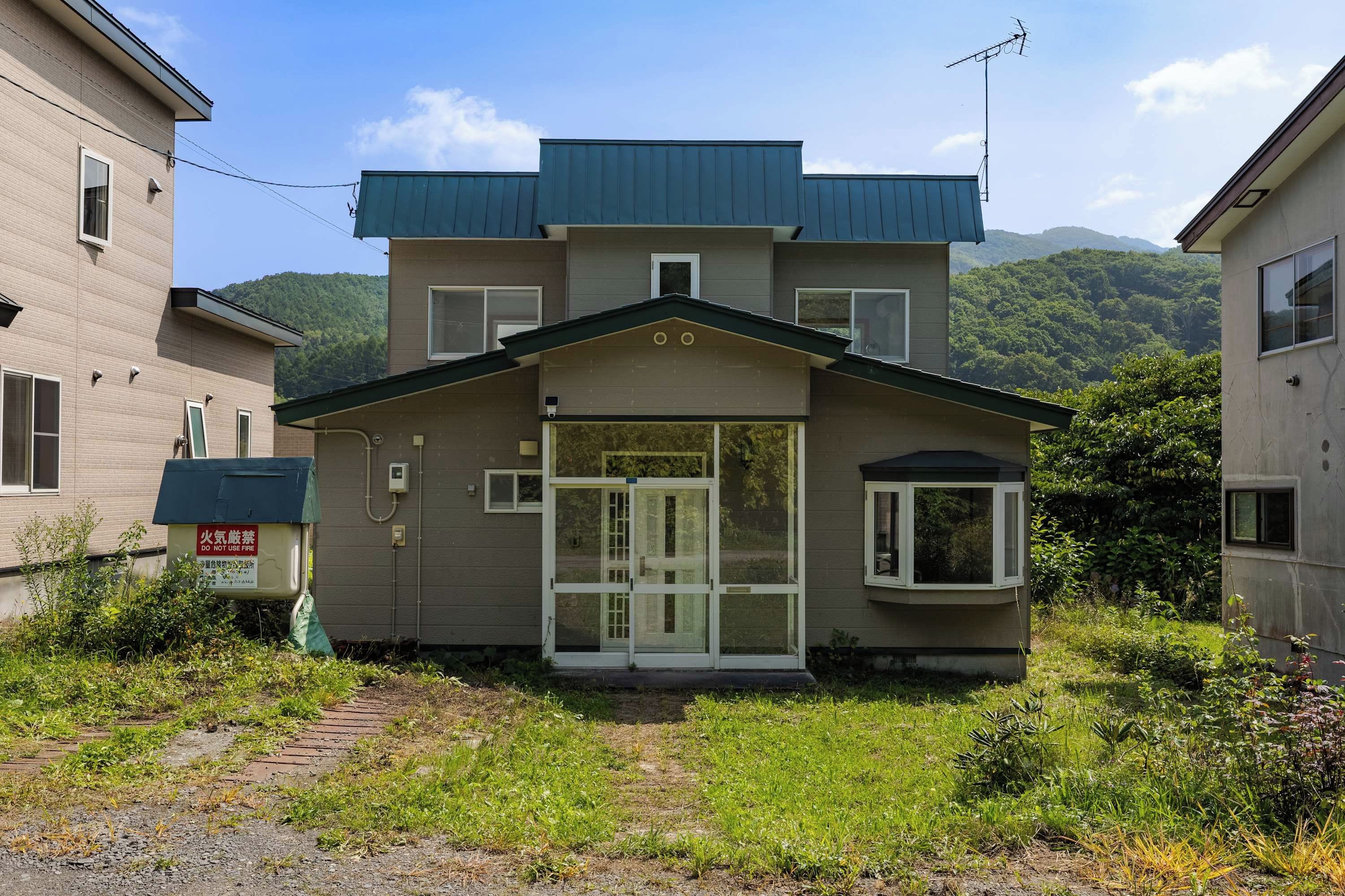 A two-story residential building with a front entrance, a small porch, and a visible satellite dish.