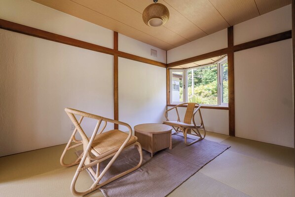 Een traditionele Japanse kamer met tatami vloeren, twee zitmanden van tatami, een klein tatami tafeltje en een raam met uitzicht op groen.