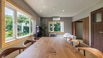 Une salle de conférence avec une longue table en bois, quatre chaises, un téléviseur et de grandes fenêtres donnant sur un paysage verdoyant.