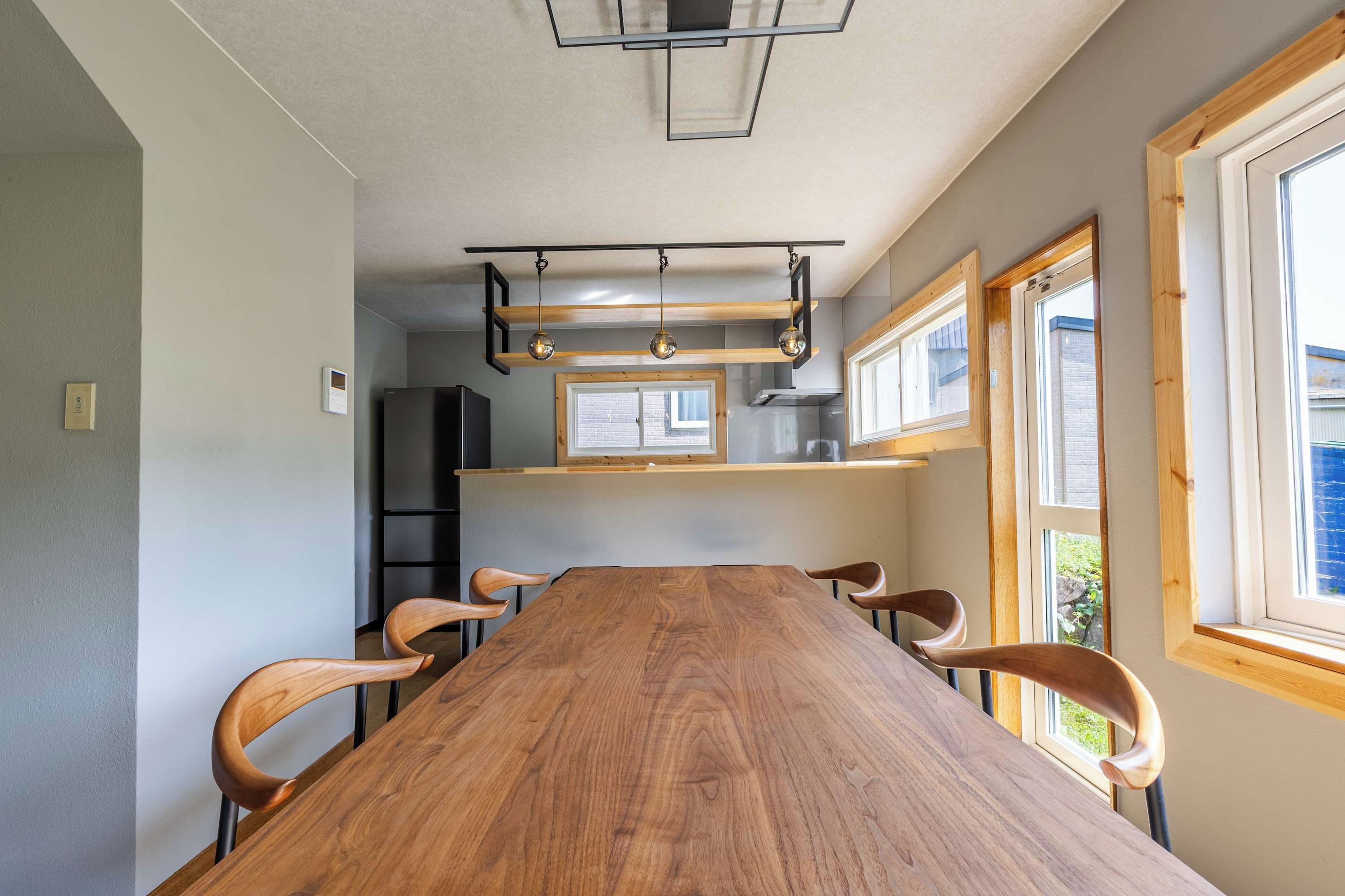 Ein Essbereich mit einem langen Holztisch, vier Stühlen, Pendelleuchten und großen Fenstern.