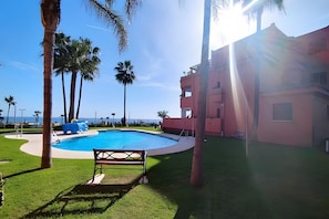 Una piscina rodeada de palmeras, un banco y un edificio con fachada rosa.