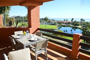 Un balcón con mesa lista para comer, con vista a un campo de golf y una extensión de agua.
