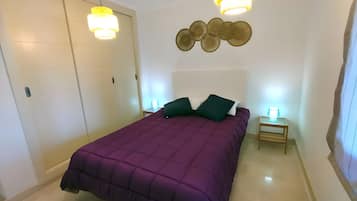 Une chambre à coucher comprenant un lit, deux tables de chevet, une armoire et un luminaire fixé au mur.