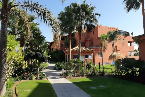 Un sendero conduce a un edificio de estilo arquitectónico tradicional, rodeado de abundante vegetación y palmeras.