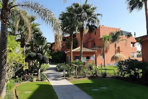 Un sendero conduce a un edificio de estilo arquitectónico tradicional, rodeado de abundante vegetación y palmeras.