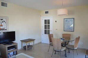 A living room with a television, a small table, wicker chairs, a glass table, and a door with frosted glass panels.