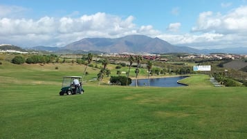 A golf course with a pond, palm trees, and mountains in the background.
