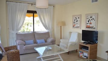 A living room with a sofa, armchair, TV stand, and a glass coffee table.