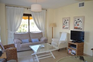 A living room with a sofa, armchair, TV stand, and a glass coffee table.