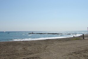 A sandy beach with a rocky outcrop in the water, a clear sky, and a distant sailboat.