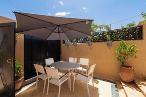 Eine Terrasse im Freien mit einem runden Tisch und Stühlen, einem großen Sonnenschirm und einem Blumentopf.
