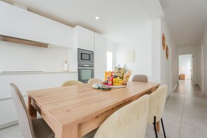 A modern kitchen with white cabinetry, a built-in oven, and a wooden dining table with chairs. - Casa Marlena- Private Terrace- 4 min to the beach by Lanzarote Vacation Homes (Puerto del Carmen)