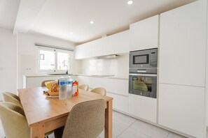 A modern kitchen with white cabinets, a wooden dining table, and a built-in oven. - Casa Marlena- Private Terrace- 4 min to the beach by Lanzarote Vacation Homes (Puerto del Carmen)
