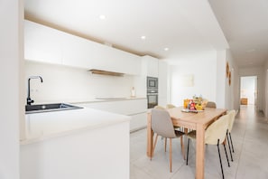 Eine moderne Küche mit weißen Schränken, einem eingebauten Ofen und einem Essbereich mit einem Holztisch und Stühlen.