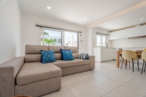 Ein modernes Wohnzimmer mit einer Couch, einem Esstisch mit Stühlen und einer Küchenzeile.
