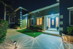 A modern house with a well-lit entrance, a green lawn, and a paved driveway. - Spacious 5BR Aruba Retreat with 2 Private Pools, Guest Apartment, 2 BBQ's & Outdoor Lounge (Noord)