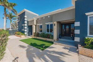A modern two-story house with a well-maintained lawn, a driveway, and a front porch. - Spacious 5BR Aruba Retreat with 2 Private Pools, Guest Apartment, 2 BBQ's & Outdoor Lounge (Noord)