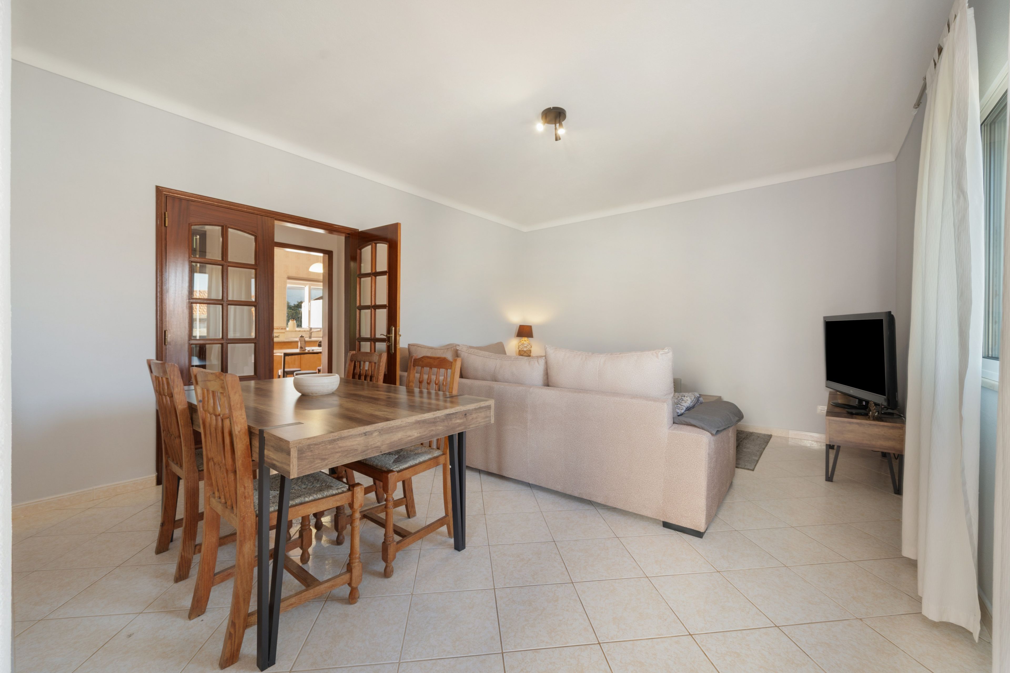 A living room with a dining table, chairs, a sofa, a TV, and a lamp.