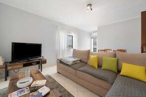 A modern living room with a flat-screen TV, a sofa, a coffee table, and a bookshelf.
