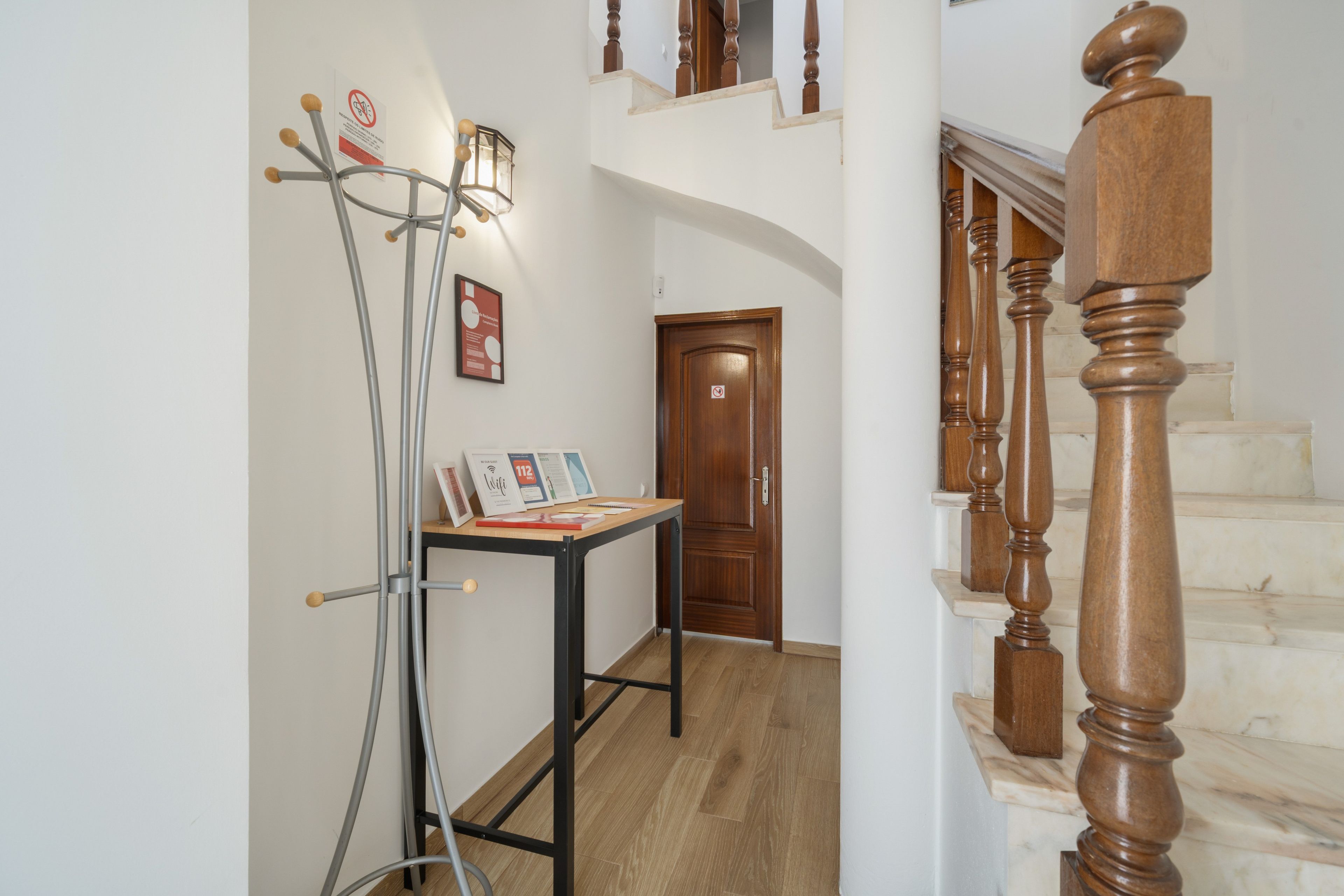 A hallway with a wooden staircase, a metal stand with a light, and a door with a 'no entry' sign.