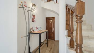 A hallway with a wooden staircase, a metal stand with a light, and a door with a 'no entry' sign.