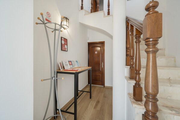 A hallway with a wooden staircase, a metal stand with a light, and a door with a 'no entry' sign.