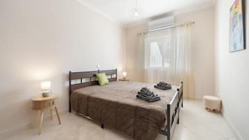 A bedroom with a bed, a nightstand, a lamp, a window with curtains, and a painting on the wall.