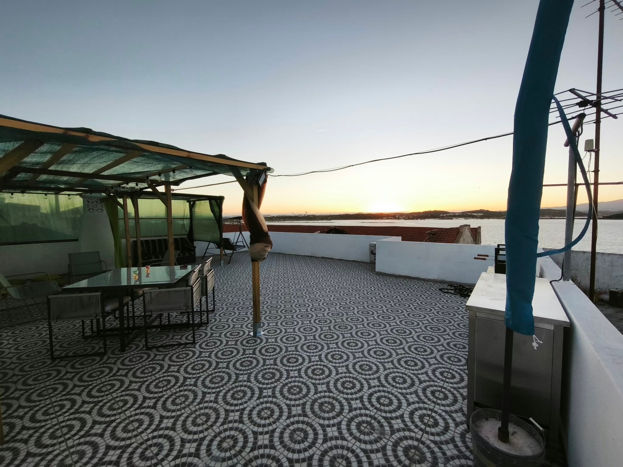 A terrace with a patterned floor, a table with chairs, and a view of a body of water at sunset.