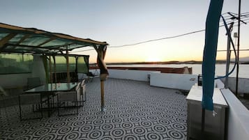 A terrace with a patterned floor, a table with chairs, and a view of a body of water at sunset.