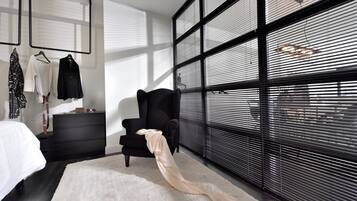 A modern bedroom with a large window, a black armchair, a white rug, and a bed with a white headboard.