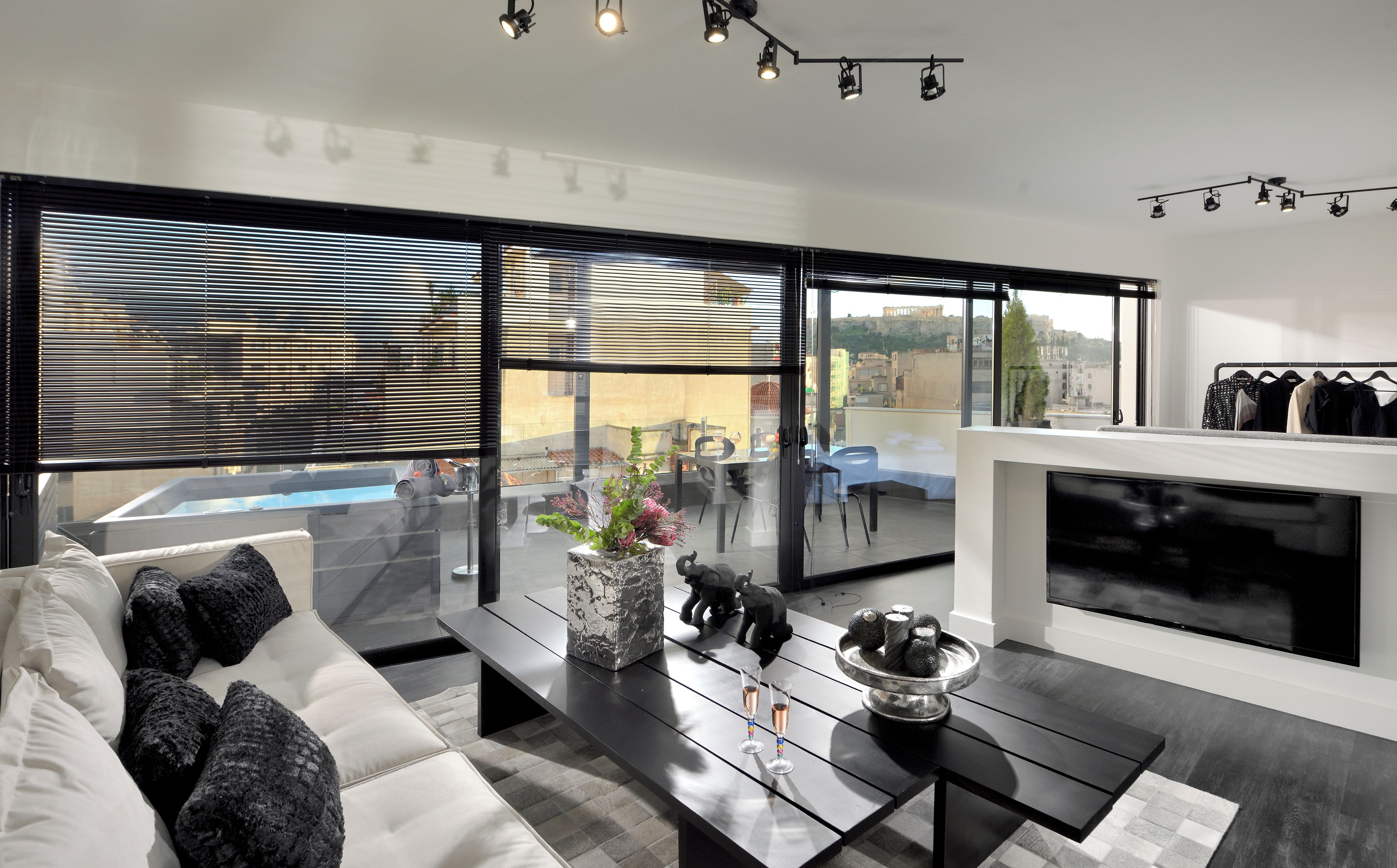 Un salon moderne avec un canapé, une table basse et une cheminée. De grandes fenêtres offrent une vue sur la ville et une piscine.