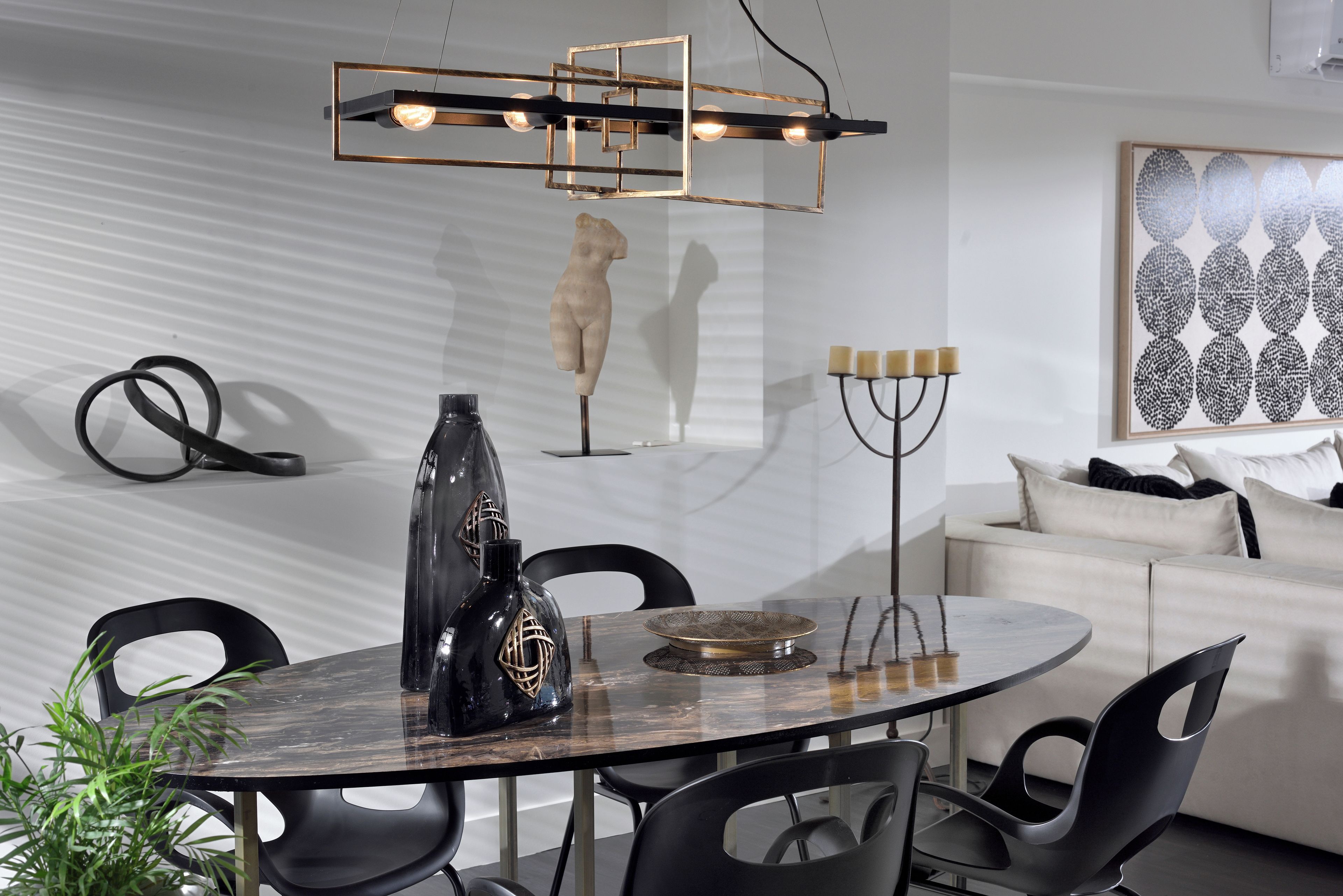 Un comedor moderno con una mesa redonda, sillas negras, un jarrón decorativo y una lámpara colgante de diseño geométrico.