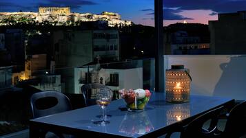 Une table avec un verre à vin, un panier de fruits et une lanterne, sur un balcon donnant sur un paysage urbain avec des bâtiments historiques.