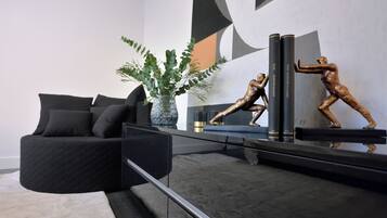 Un salon moderne avec un canapé noir, une table basse en verre et des objets décoratifs, notamment un vase avec des feuilles vertes et deux sculptures en bronze.