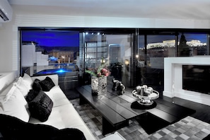 Un salon moderne avec un canapé, une table basse et une cheminée. Une grande fenêtre offre une vue sur le paysage urbain et une piscine.